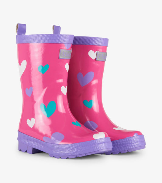 Pink rain boots with colorful heart patterns and purple accents, featuring a textured sole and pull tabs for easy wear.