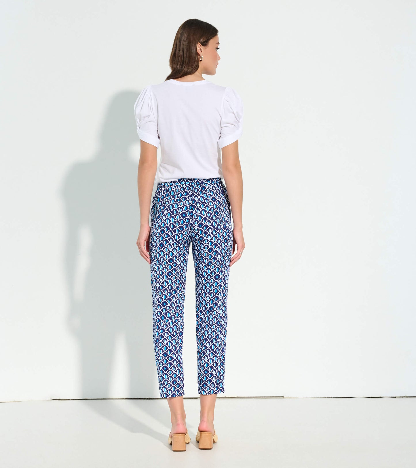 White short-sleeve tee with puffed sleeves, paired with patterned blue pants, viewed from the back.