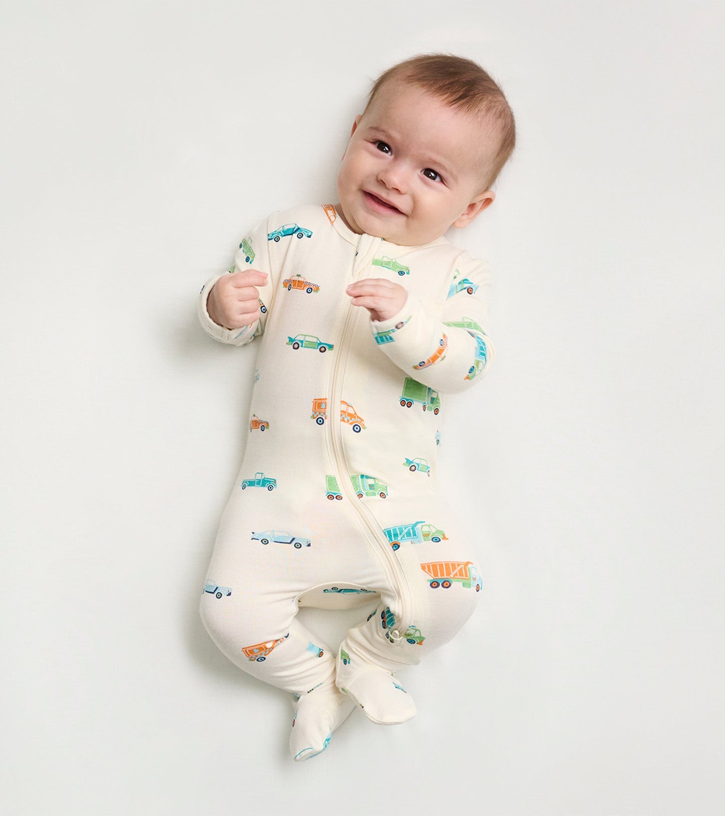 Cream footed sleeper for baby boys, featuring colorful car and truck prints, with a front zipper and footed design.