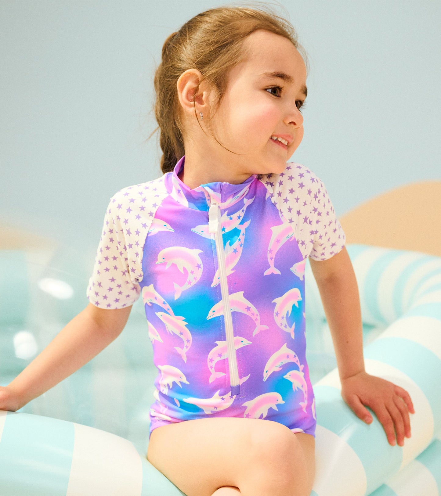 Purple one-piece rashguard featuring dolphin prints and star-patterned sleeves, ideal for swimming or beach activities.