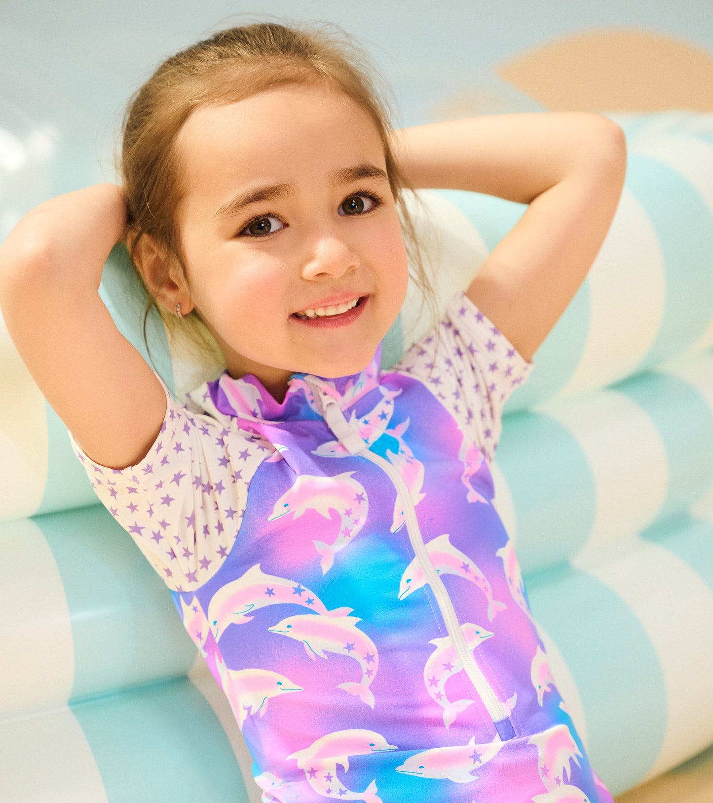 Colorful one-piece rashguard featuring dolphins and stars, designed for girls, with a zip front and short sleeves.