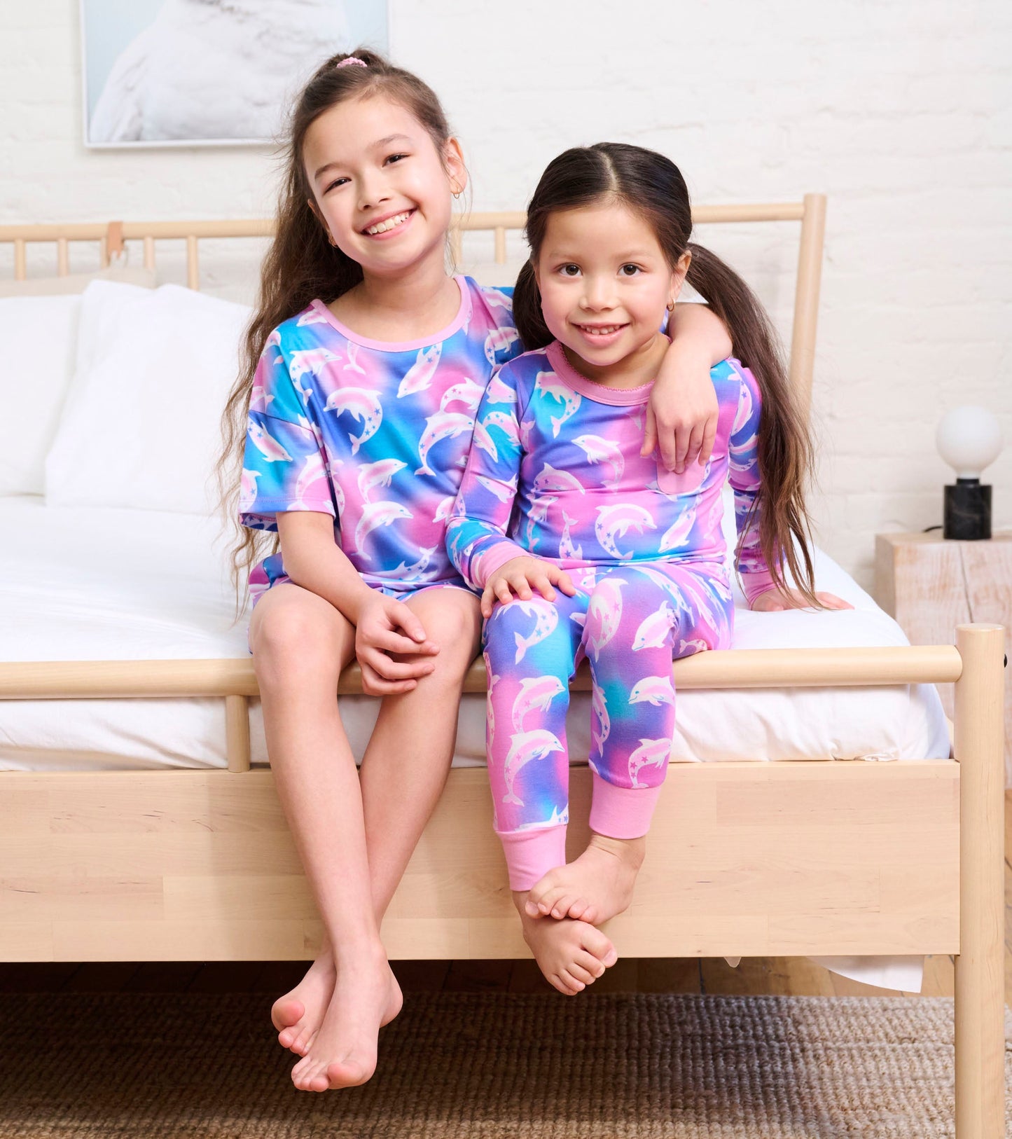Girls' bamboo pajama set featuring a colorful dolphin print, with a short-sleeve top and long pants, worn by two children.