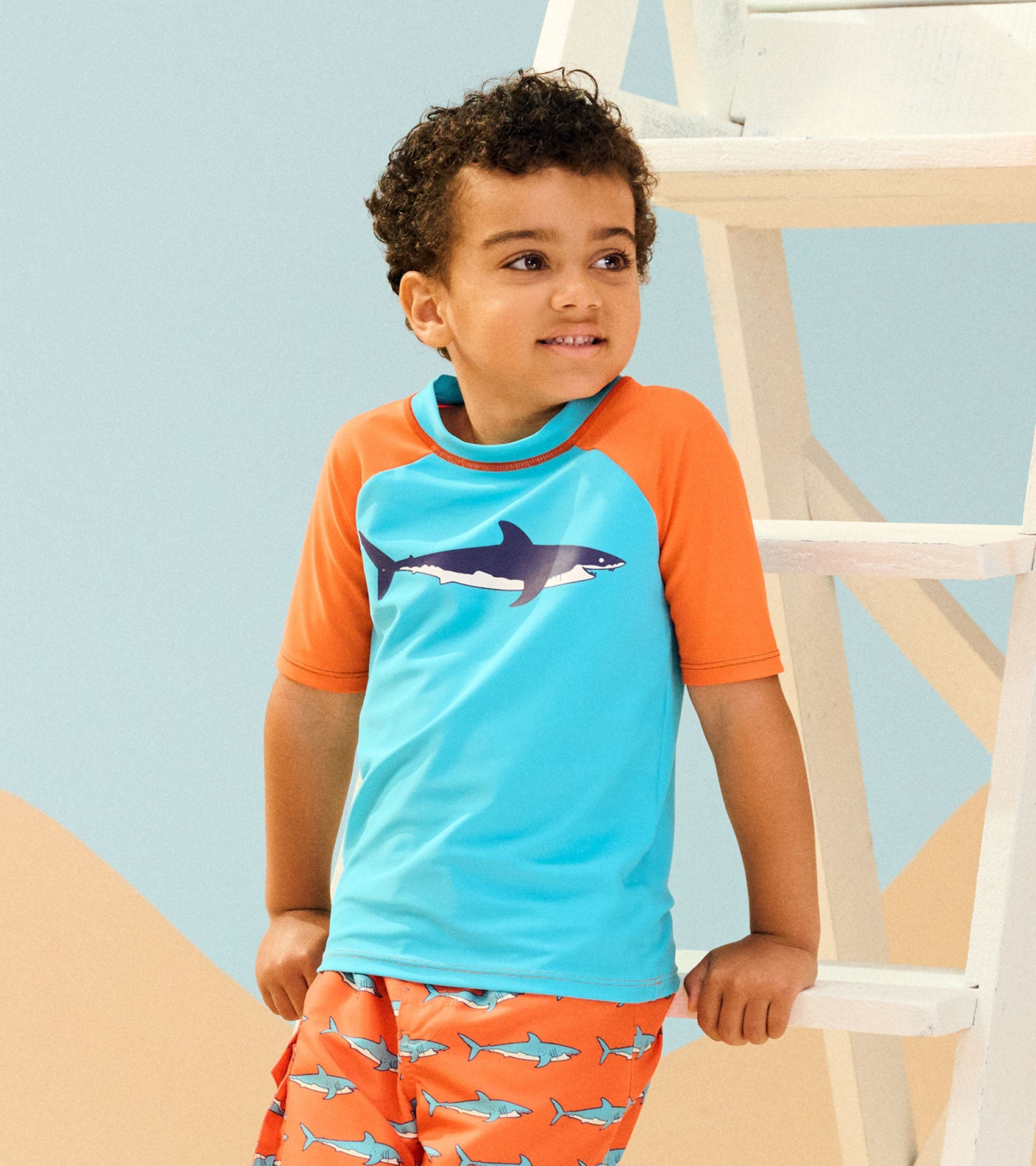 Short sleeve rashguard in turquoise with orange sleeves, featuring a shark graphic, ideal for beach or pool wear.