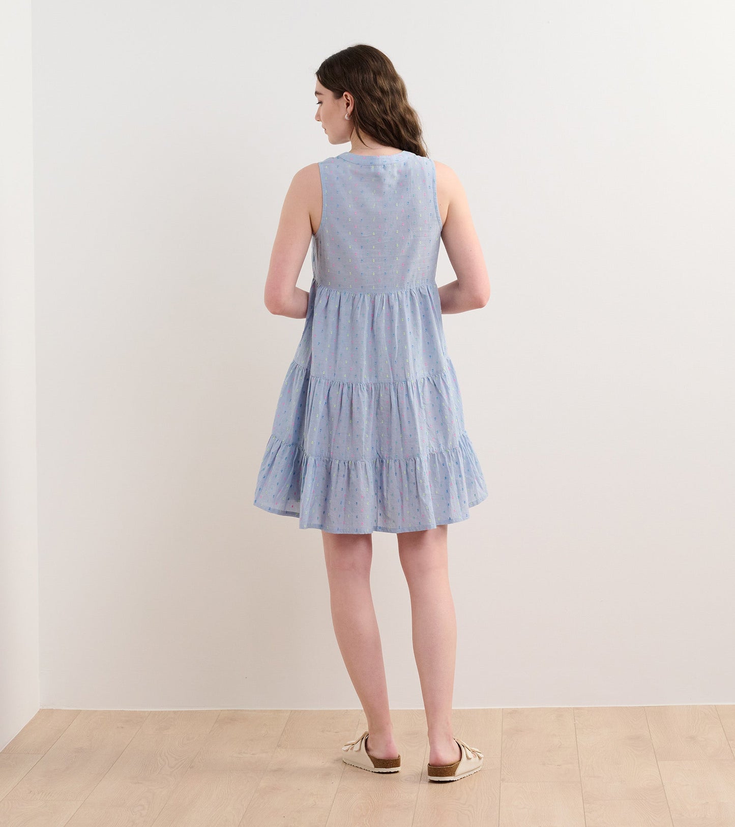 Light blue chambray dress with a tiered design and colorful spots, featuring a sleeveless cut and a relaxed fit.