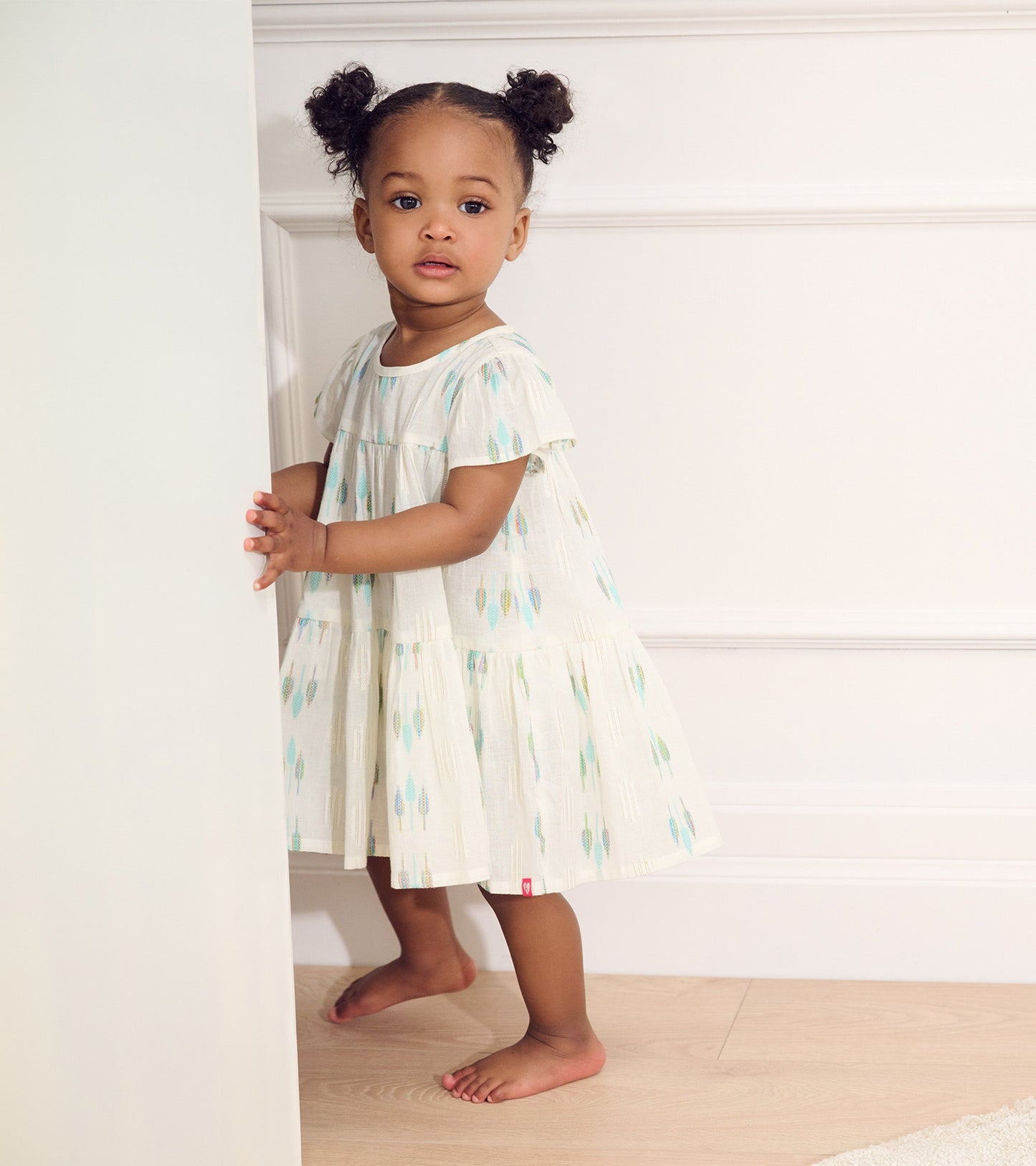 Light blue woven puff dress with colorful feather patterns, short sleeves, and a tiered skirt for baby and toddler girls.