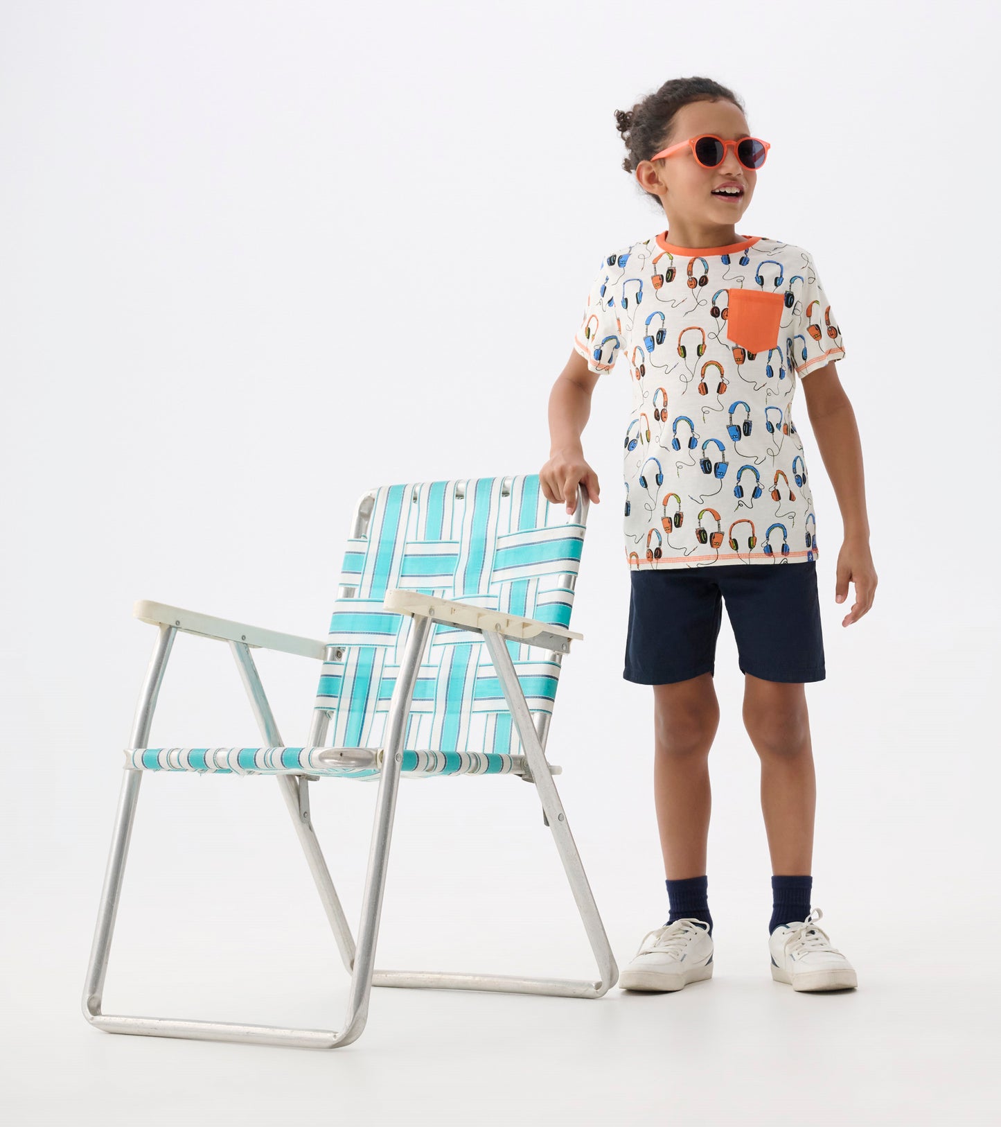 White short-sleeve t-shirt with colorful headphone print and a coral pocket, paired with navy shorts.