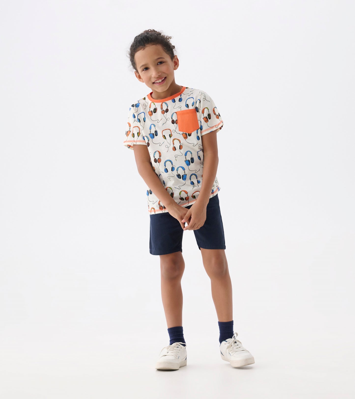 Boys' short-sleeve t-shirt featuring a colorful headphone pattern and an orange pocket, paired with navy shorts.