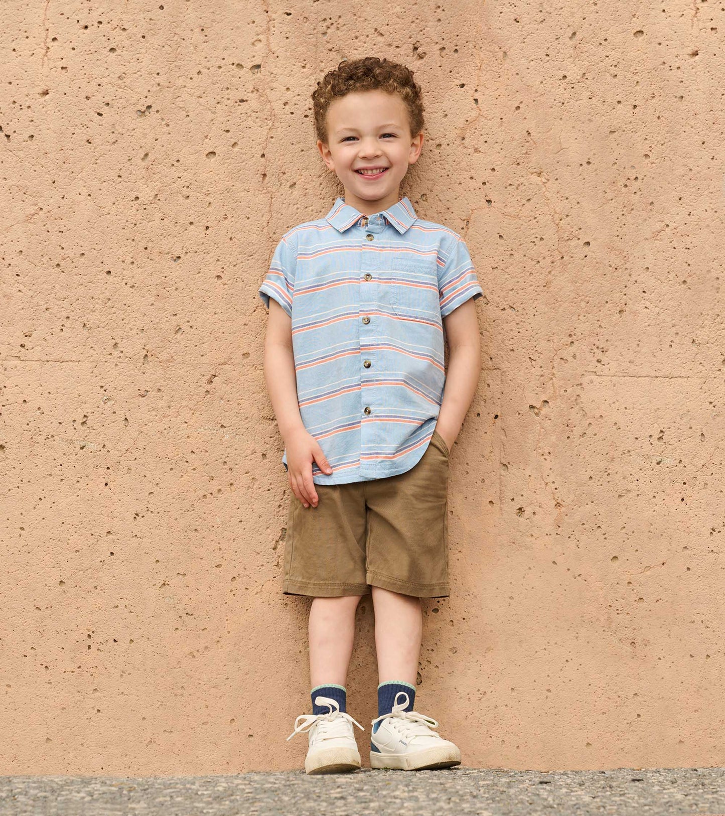 Light blue button-down shirt with colorful stripes, short sleeves, and a chest pocket, worn by a smiling boy.