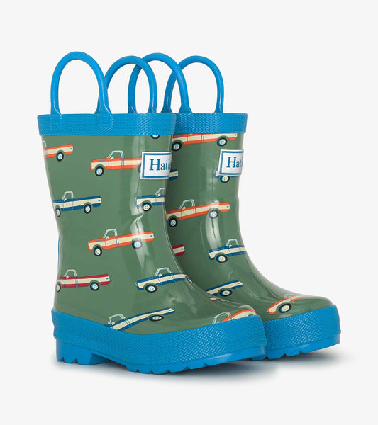 Green rain boots with blue handles, featuring colorful truck patterns, designed for boys.