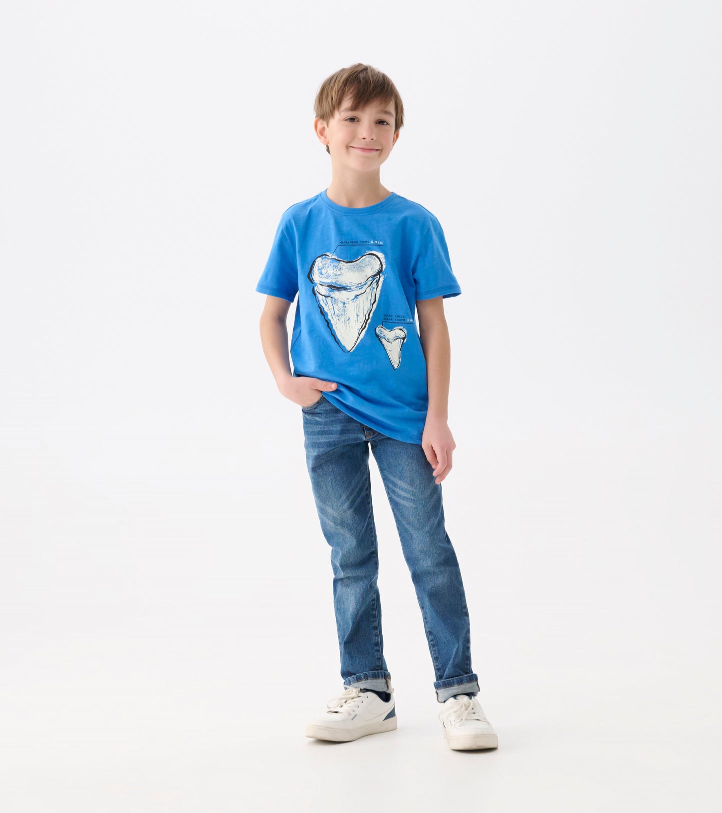 Blue graphic tee featuring shark tooth prints, short sleeves, and a relaxed fit, worn by a smiling boy with jeans.