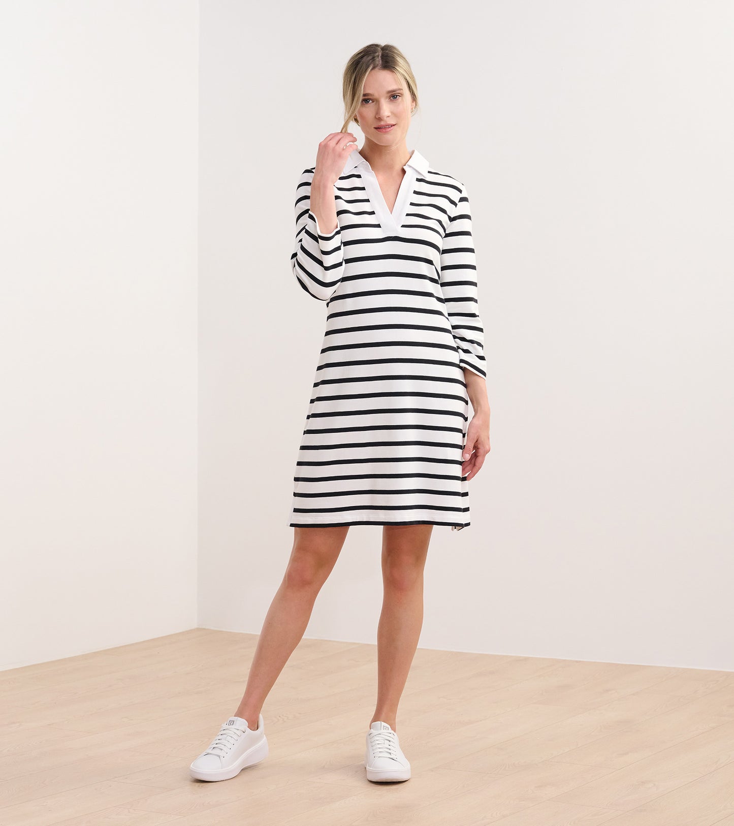 Woman wearing a white dress with black horizontal stripes, collared V-neck, and long sleeves, front view.
