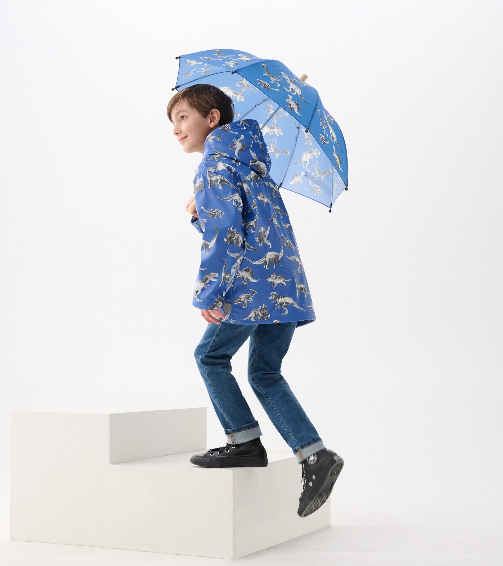 Blue zip-up rain jacket featuring a dinosaur print, worn by a boy holding a matching umbrella while climbing stairs.