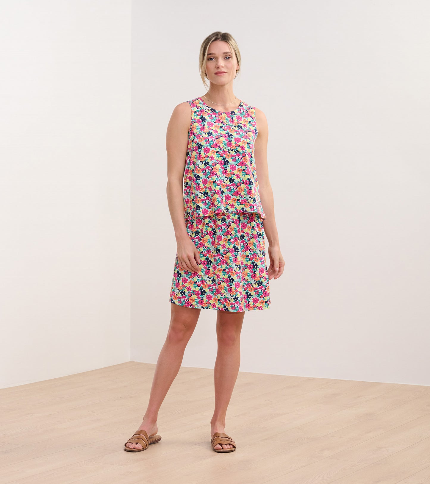 Sleeveless dress featuring a vibrant floral pattern in pink, blue, and green, with a relaxed fit and knee-length skirt.