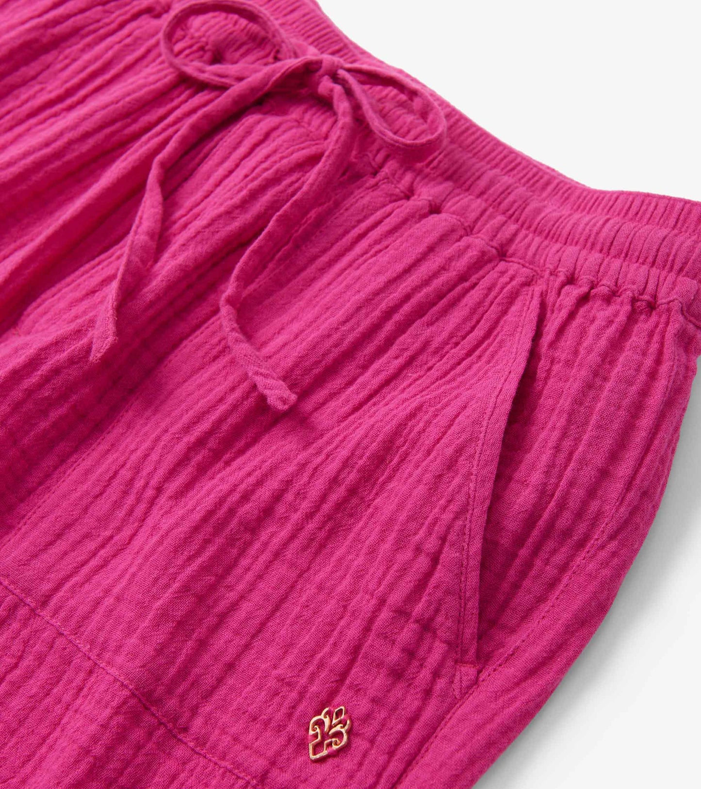 Fuchsia shorts with a textured fabric, elastic waistband, and drawstring, featuring side pockets and a small logo.