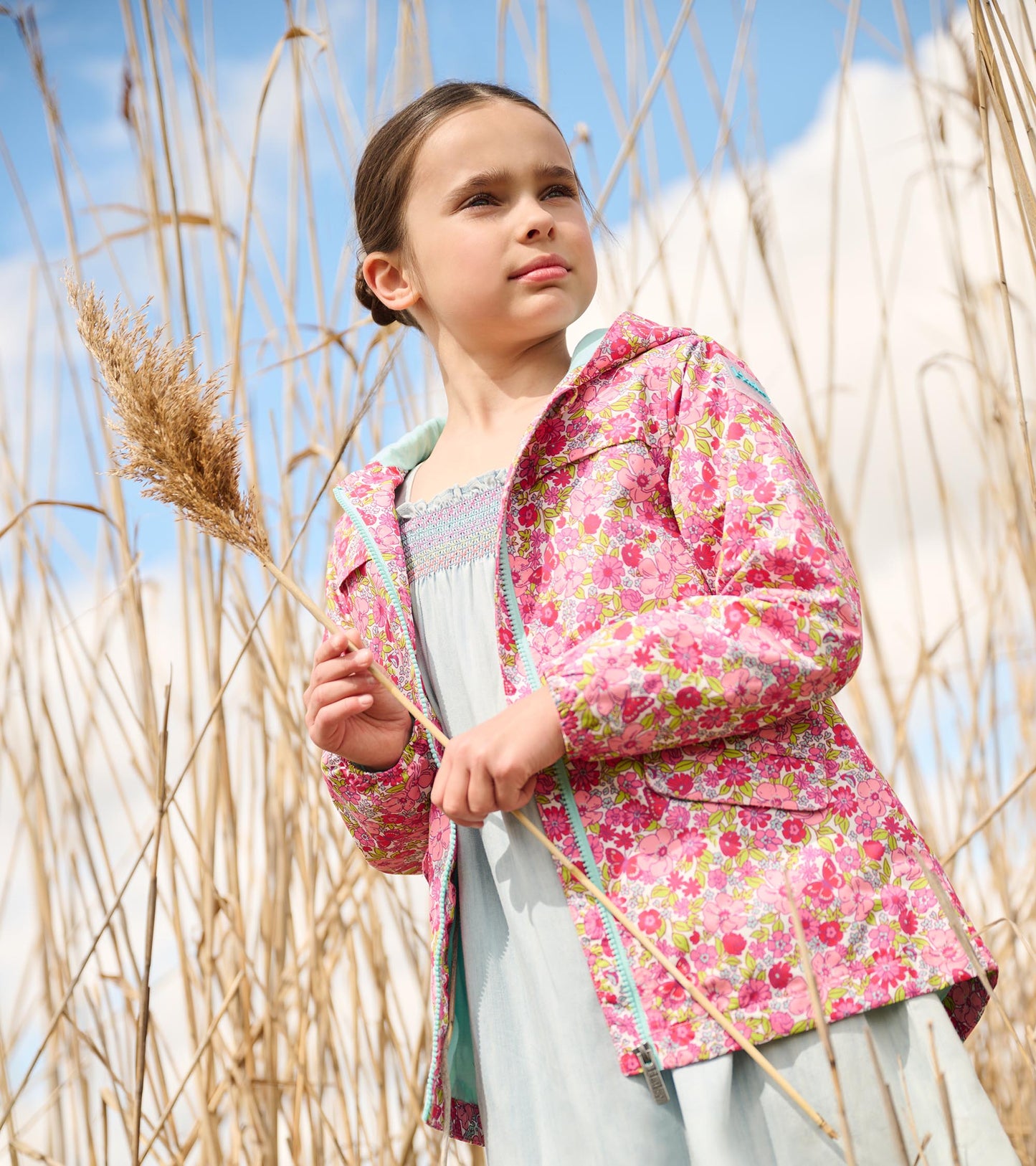 Lightweight zip-up rain jacket in pink with colorful floral pattern, worn by a girl in a natural setting.