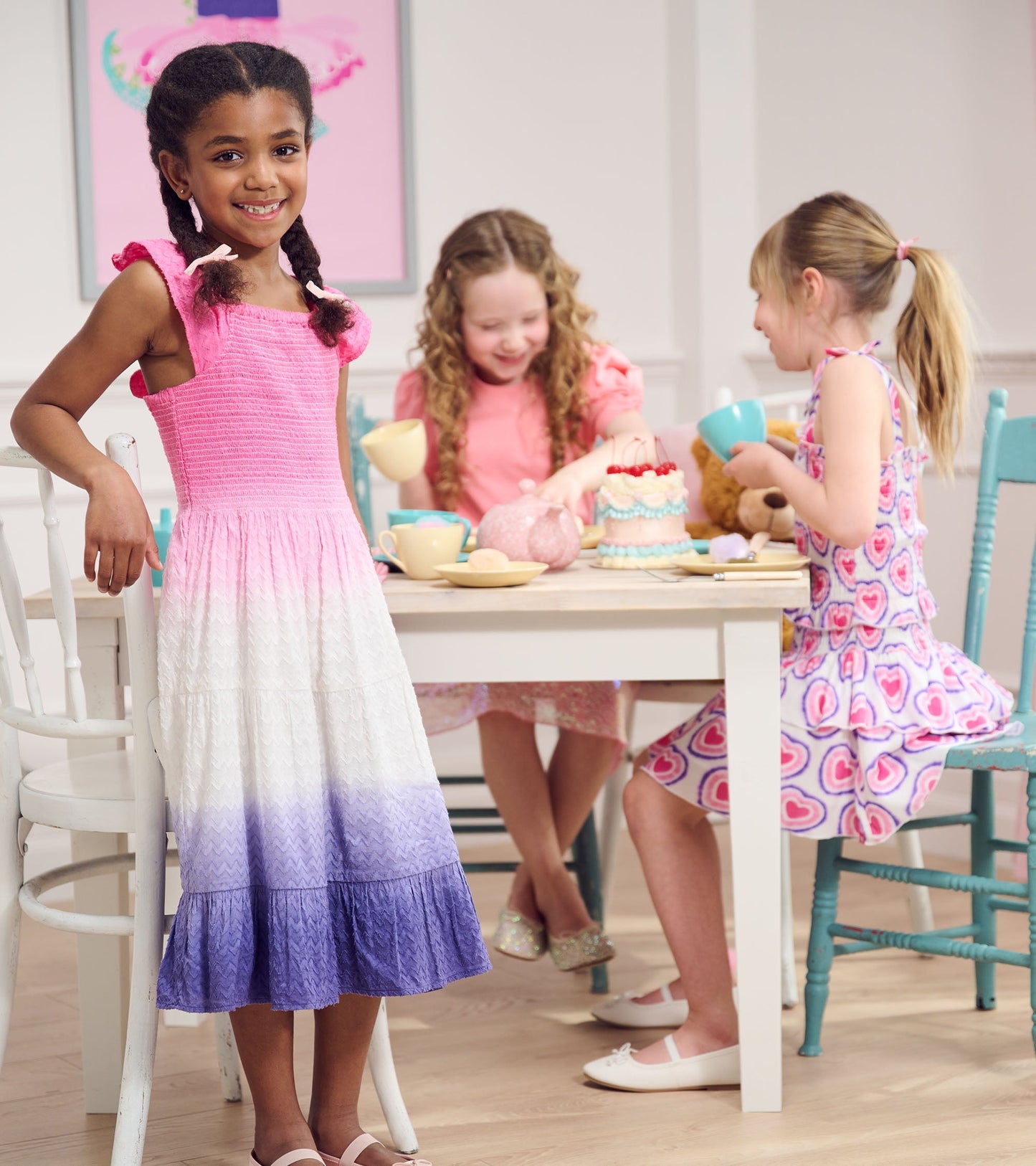 Smocked angel dress with pink, white, and purple ombre pattern, featuring ruffled straps, worn by a girl at a tea party.