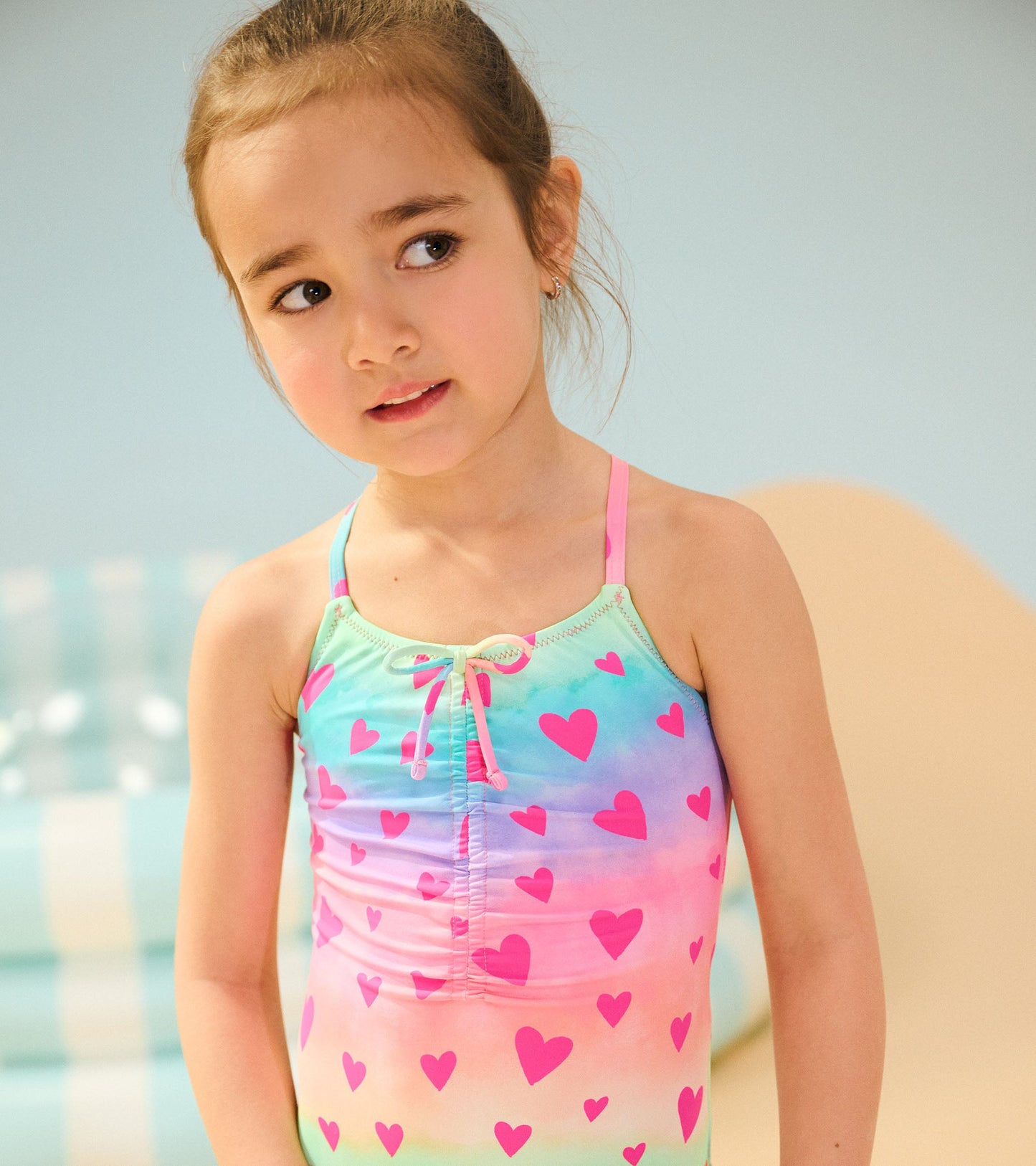 Ruched front swimsuit featuring a pastel gradient with pink heart patterns and adjustable straps.