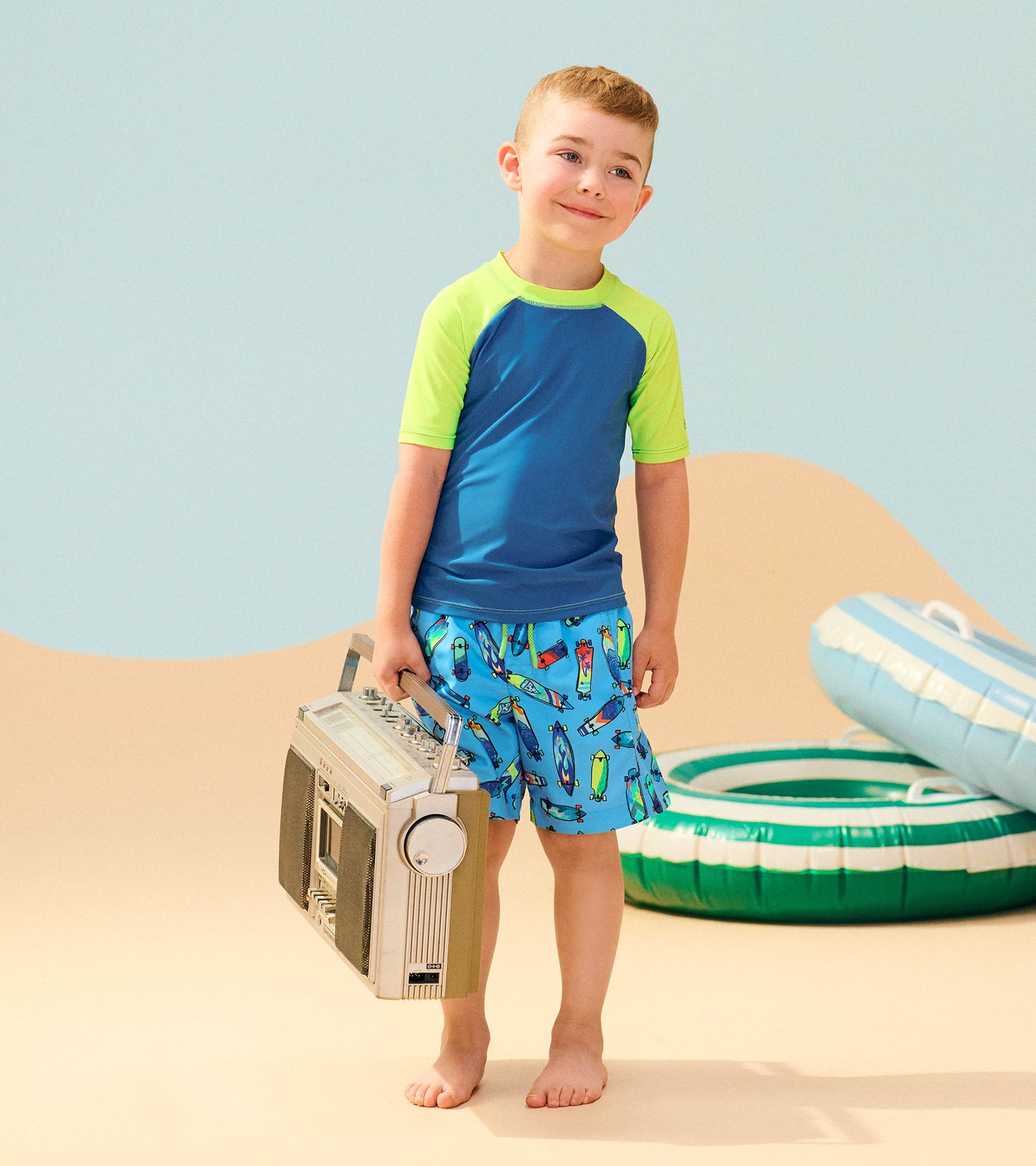 Boys' swim trunks in bright blue with colorful surfboard pattern, paired with a short-sleeve green and blue rash guard.