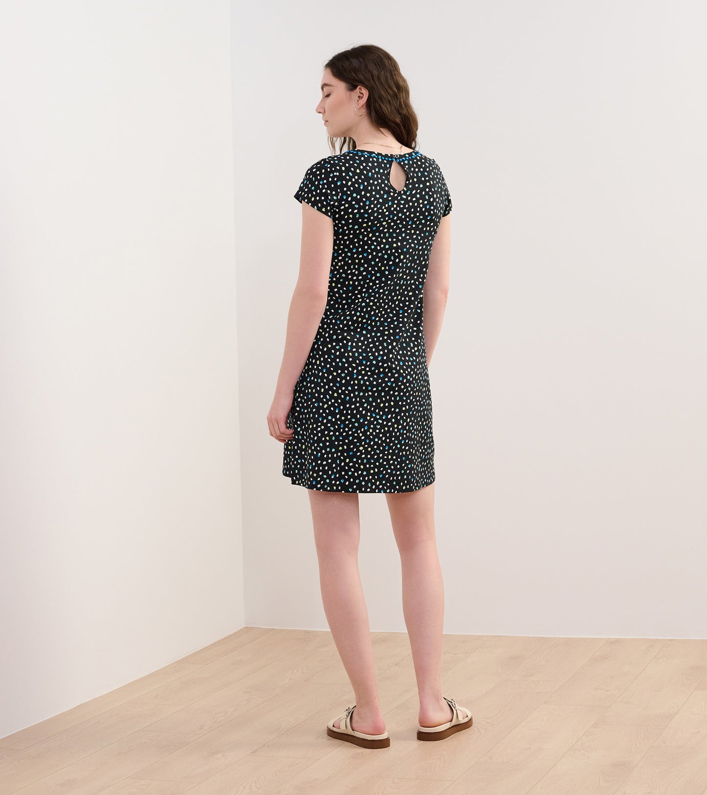Back view of a short A-line dress featuring a black fabric with colorful polka dots and a keyhole detail at the neckline.