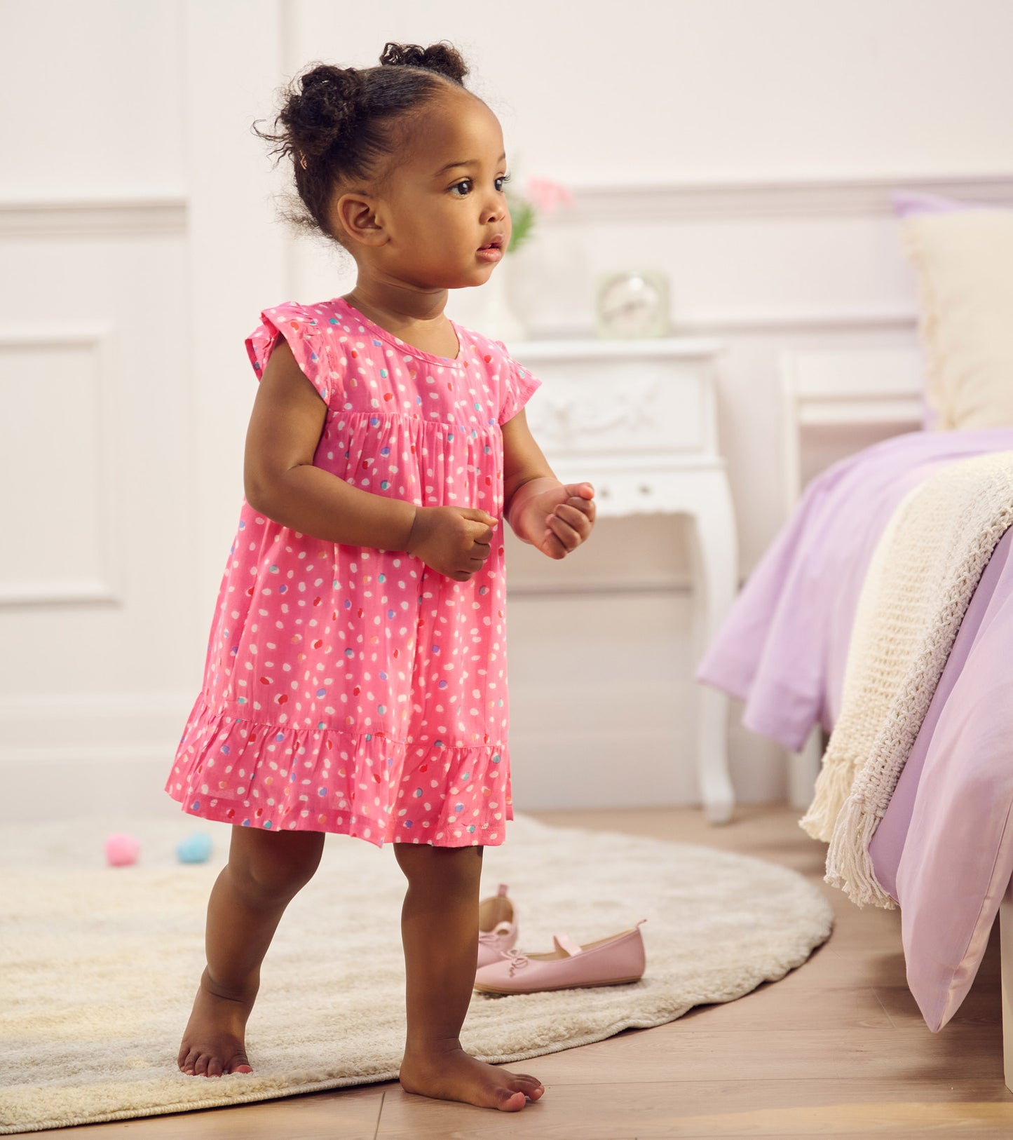 Toddler girl wearing a pink polka dot flounce dress with short ruffled sleeves and tiered hem