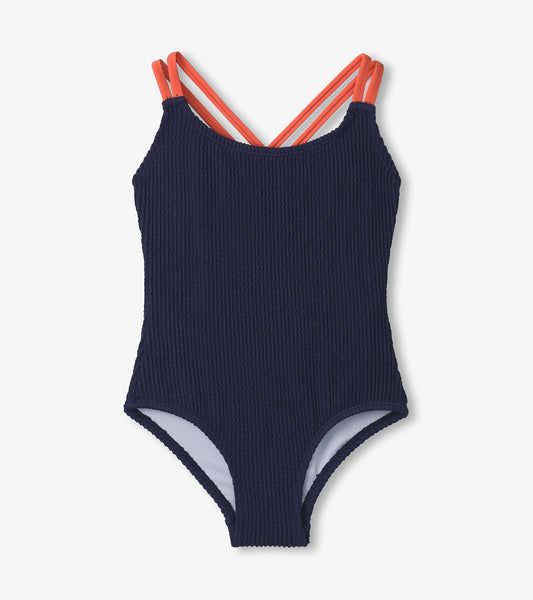 Patriot blue ribbed swimsuit with coral cross straps, designed for girls, featuring a classic one-piece silhouette.