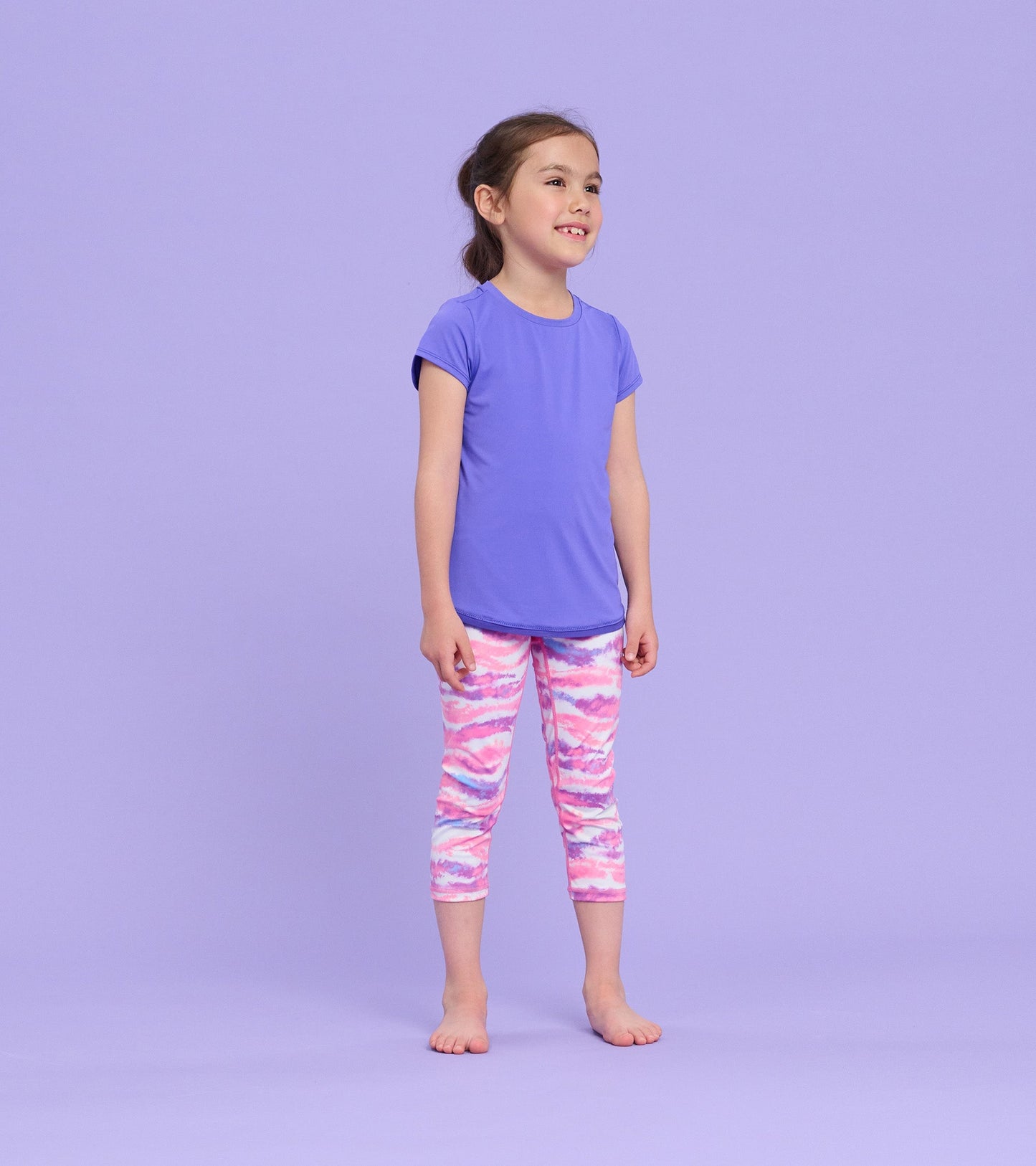 Purple short-sleeve T-shirt with a smooth texture, worn by a girl standing against a light purple background.