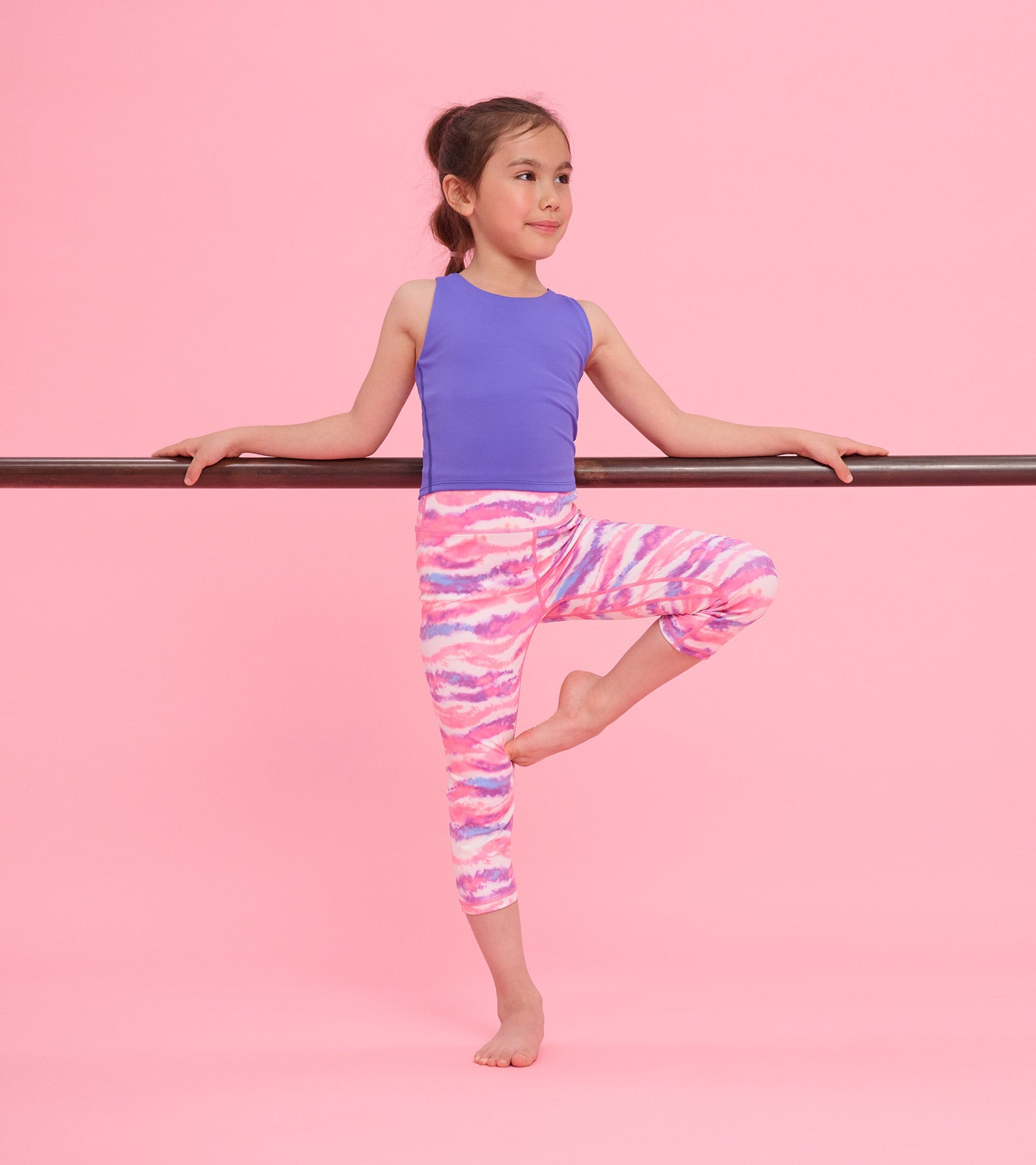 Purple tank top on a girl, paired with colorful patterned leggings, posing against a pink background.