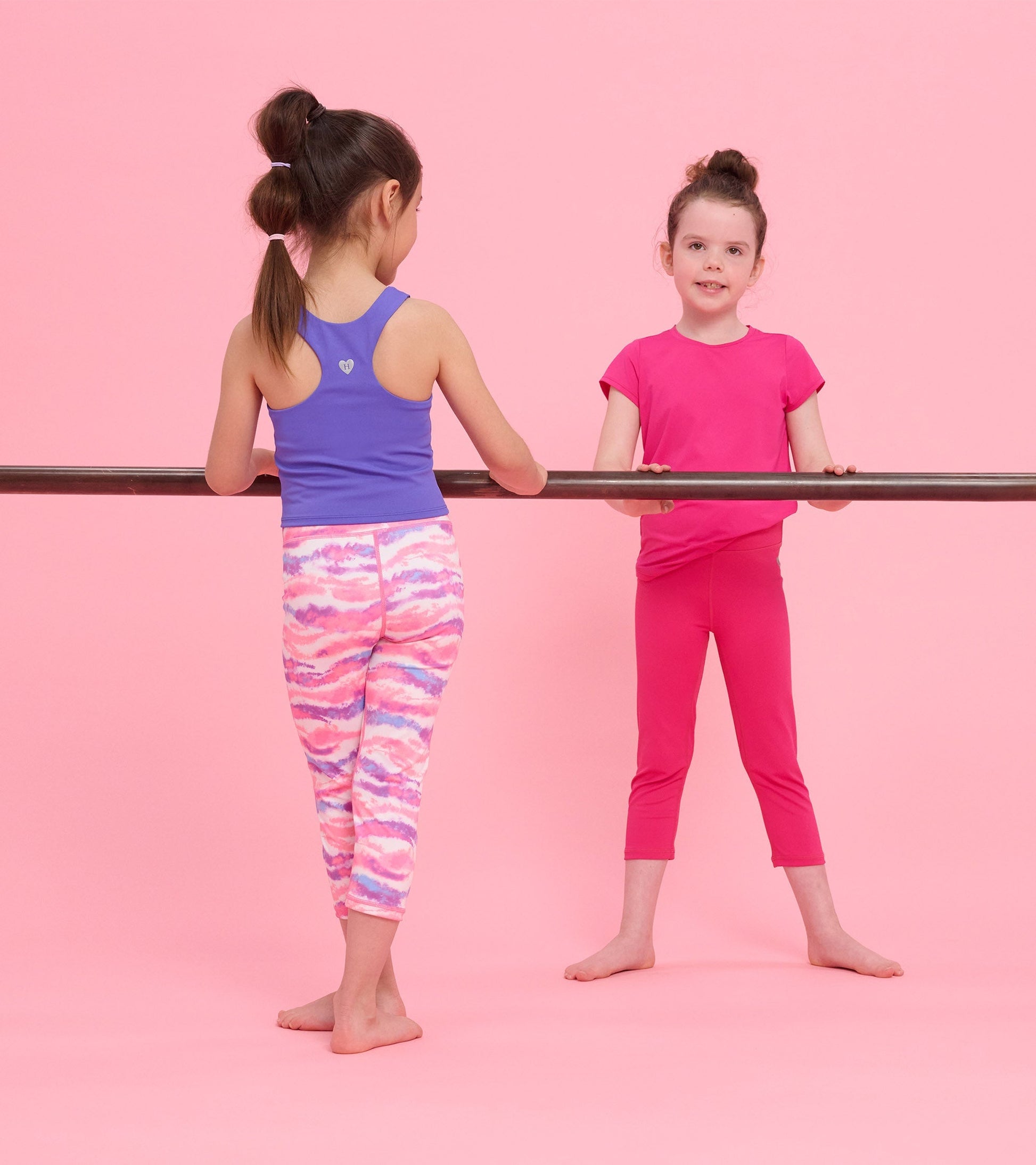 Purple tank top on a girl, paired with colorful patterned leggings, against a pink background.