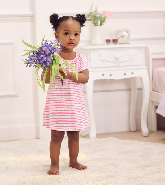 Pink and white striped raglan dress with cherry print, worn by a toddler holding purple flowers, standing on a soft rug.