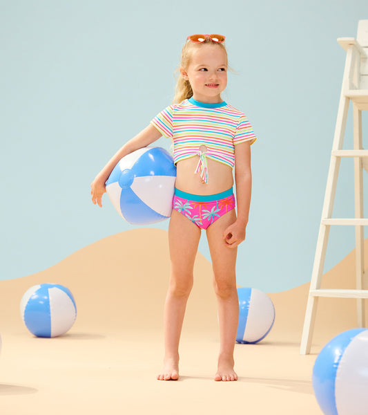 Colorful striped short sleeve tankini with palm print bottoms, perfect for beach play, worn by a girl holding a beach ball.