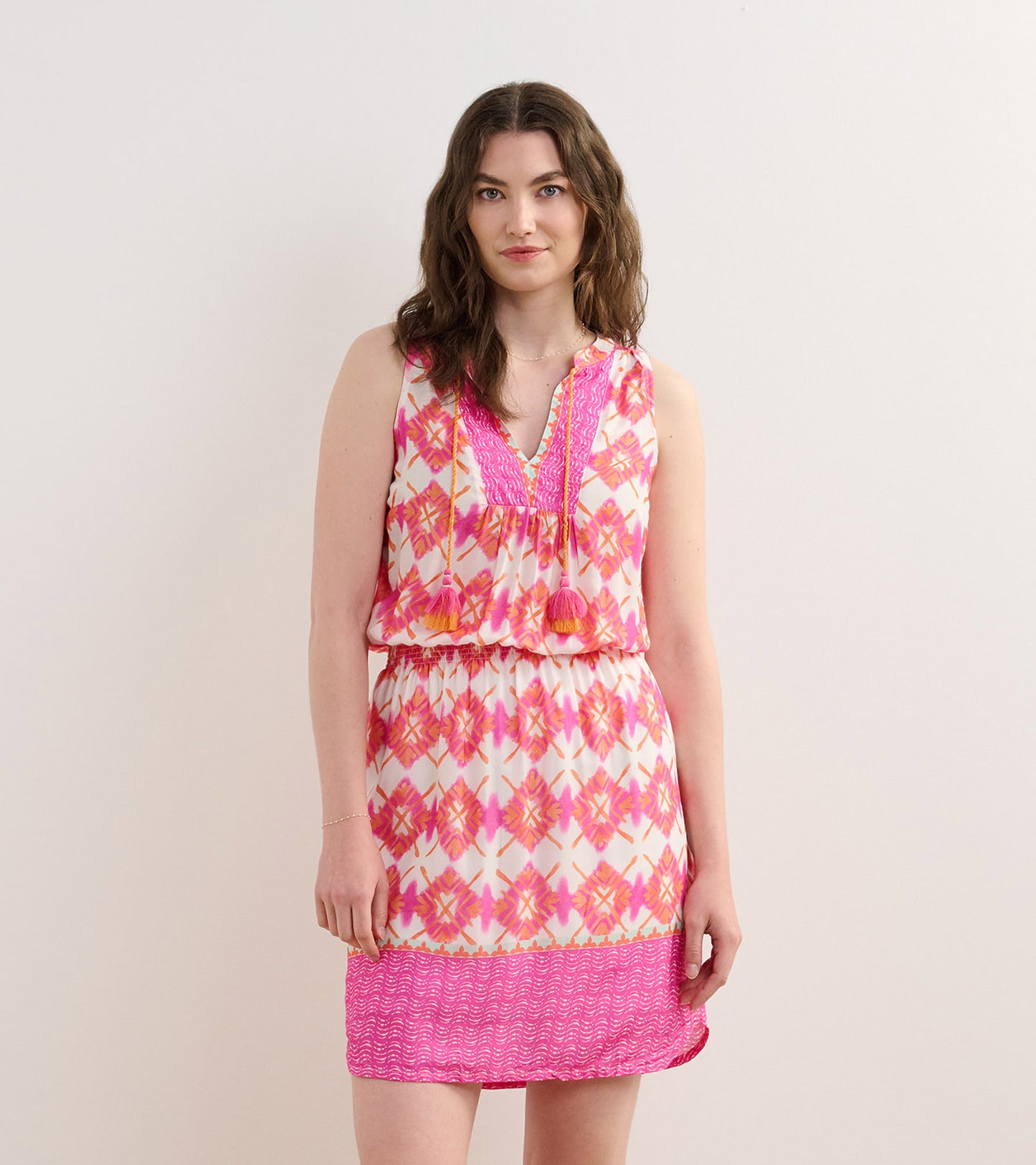 Sleeveless dress featuring a vibrant pink and white sunburst pattern with tassel details and an elastic waist.