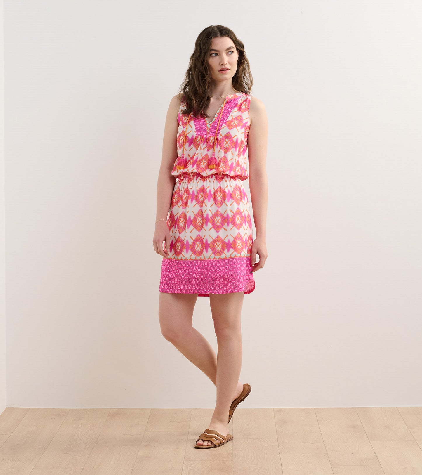 Sleeveless pink dress with a geometric pattern, gathered waist, and a flared skirt, styled with sandals.
