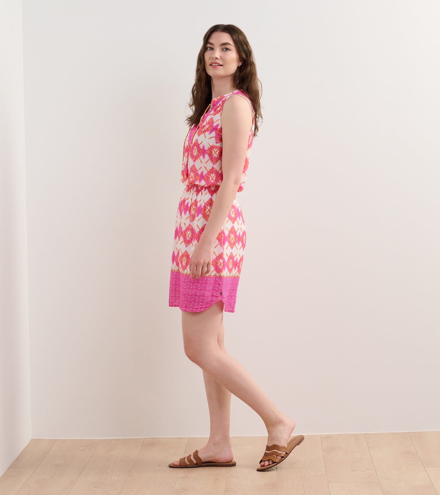 Sleeveless pink and white dress with a geometric pattern, cinched waist, and a flared hem, styled with sandals.