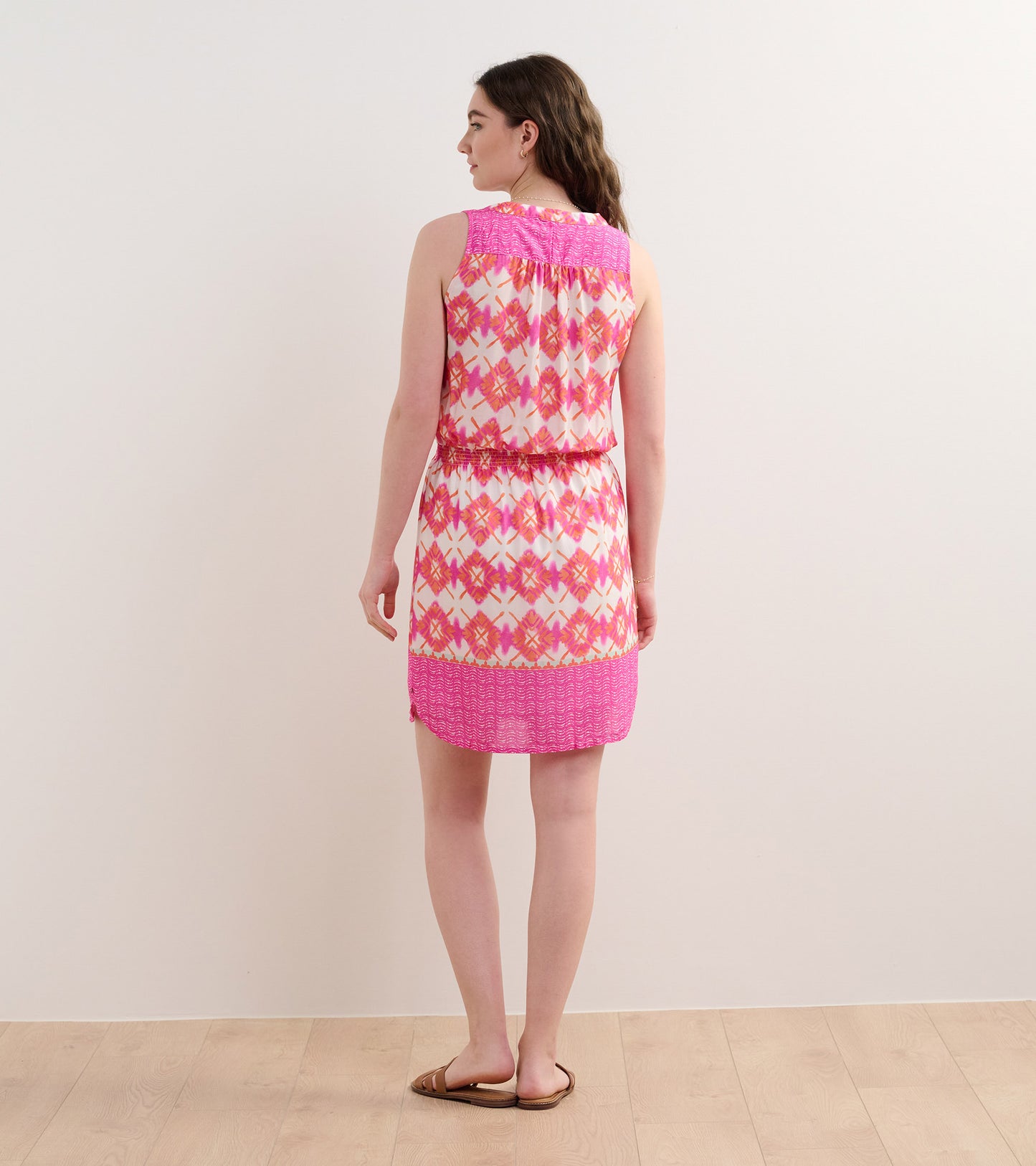 Sleeveless dress featuring a colorful sunburst pattern in pink and white, with a cinched waist and a relaxed fit.