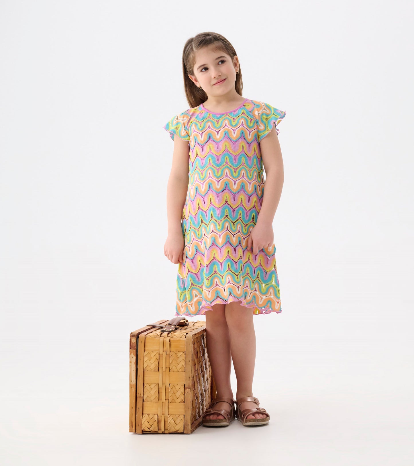 Colorful crochet dress featuring a wavy rainbow pattern, short flutter sleeves, and a relaxed fit, paired with a wicker suit…