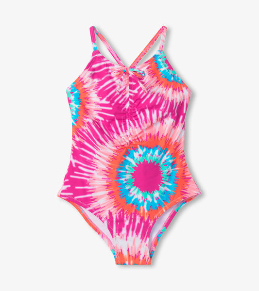 Bright pink tie-dye swimsuit with ruched front and crisscross straps, featuring colorful sunburst patterns.