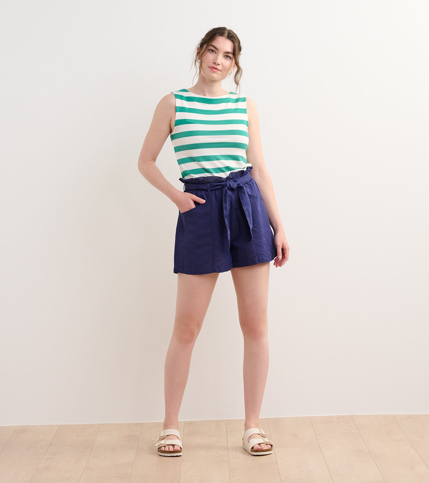 Sea green and white striped tank top, sleeveless design, paired with navy shorts, model standing on a light wooden floor.