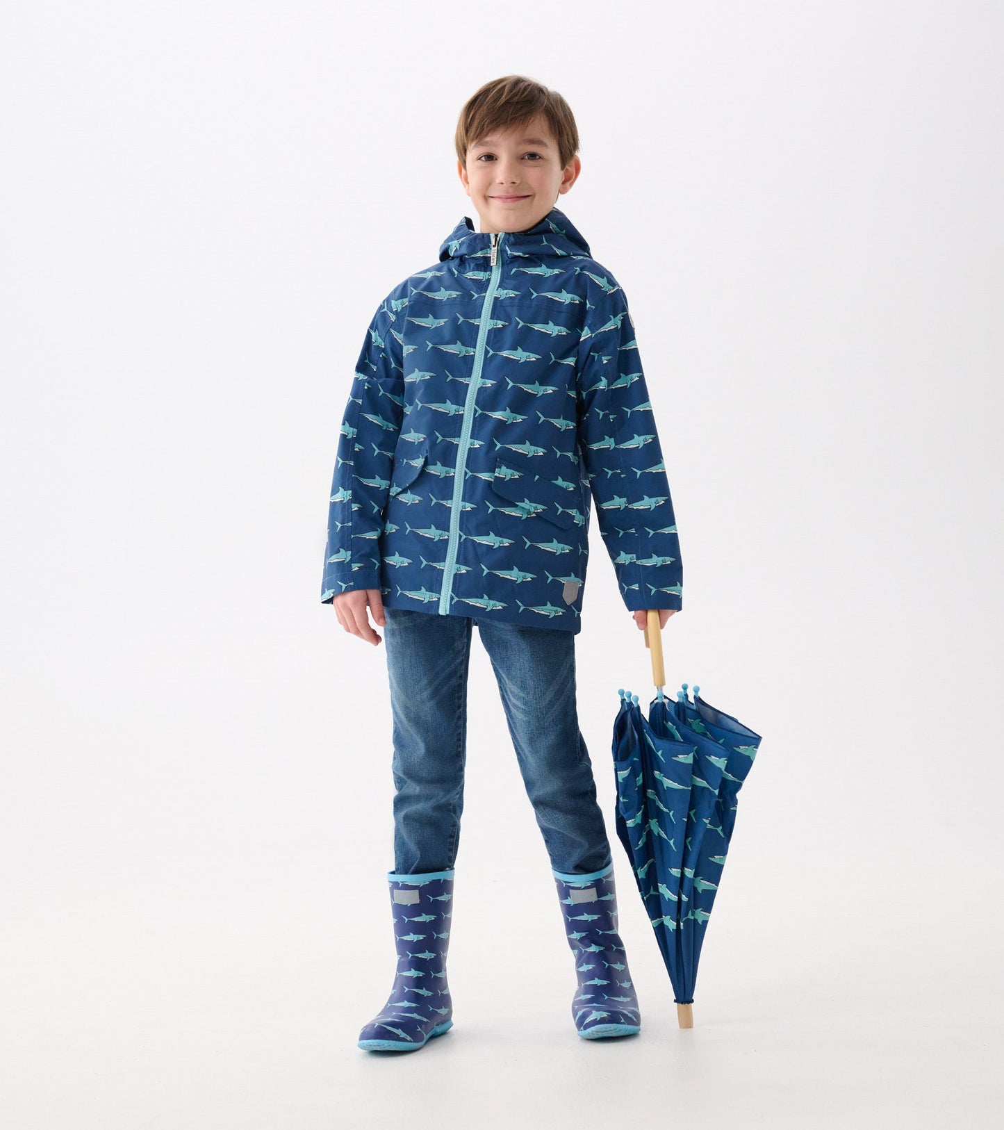 Lightweight navy rain jacket with shark pattern, hood, and zip-up front, paired with blue jeans and matching umbrella.