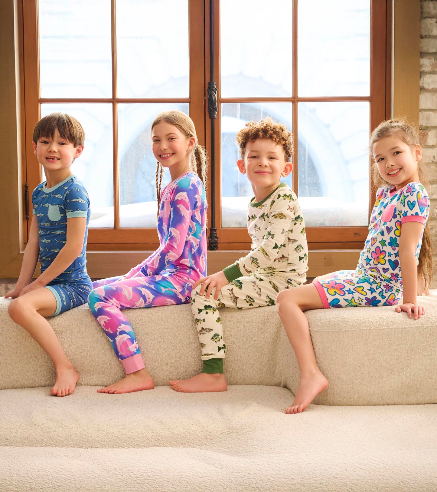 Four children sit on a couch wearing colorful bamboo short pajama sets with various fun patterns.