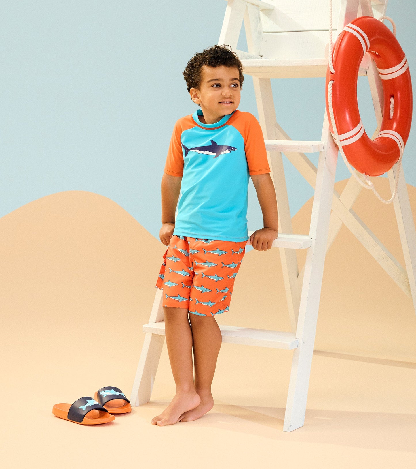 Boys' board shorts featuring an orange shark pattern, paired with a blue and orange short-sleeve rash guard.