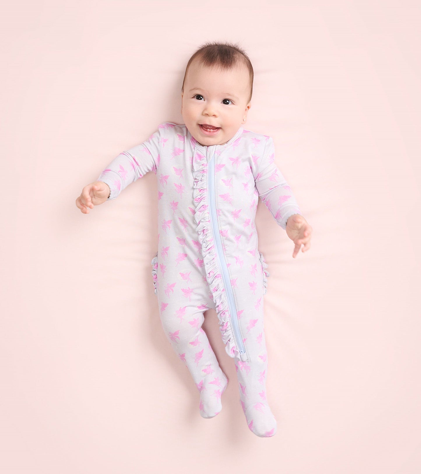 Light gray footed sleeper with pink fairy print and ruffle detail, suitable for baby girls, shown on a soft background.