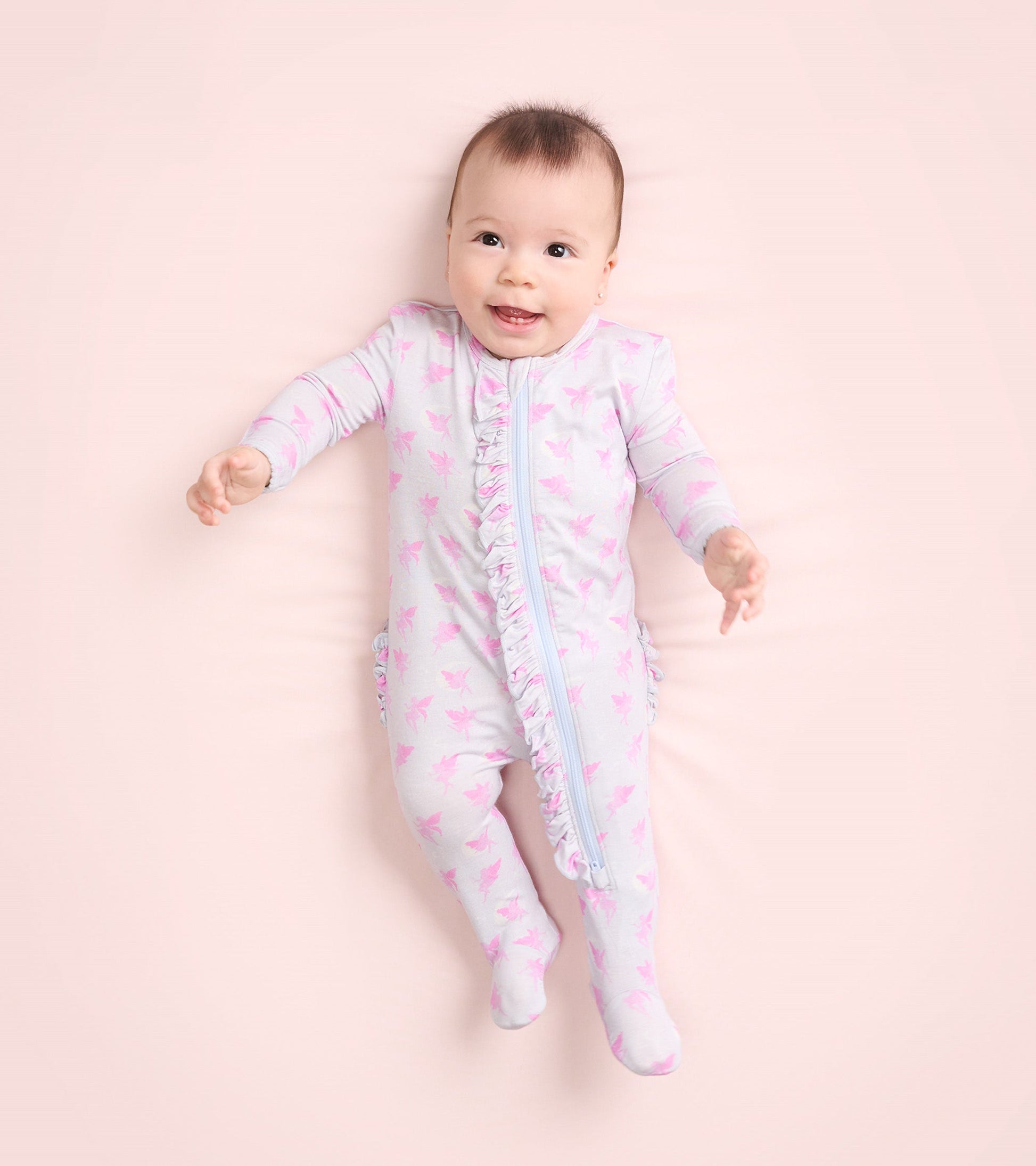 Light gray footed sleeper with pink fairy print and ruffle detail, suitable for baby girls, shown on a soft background.