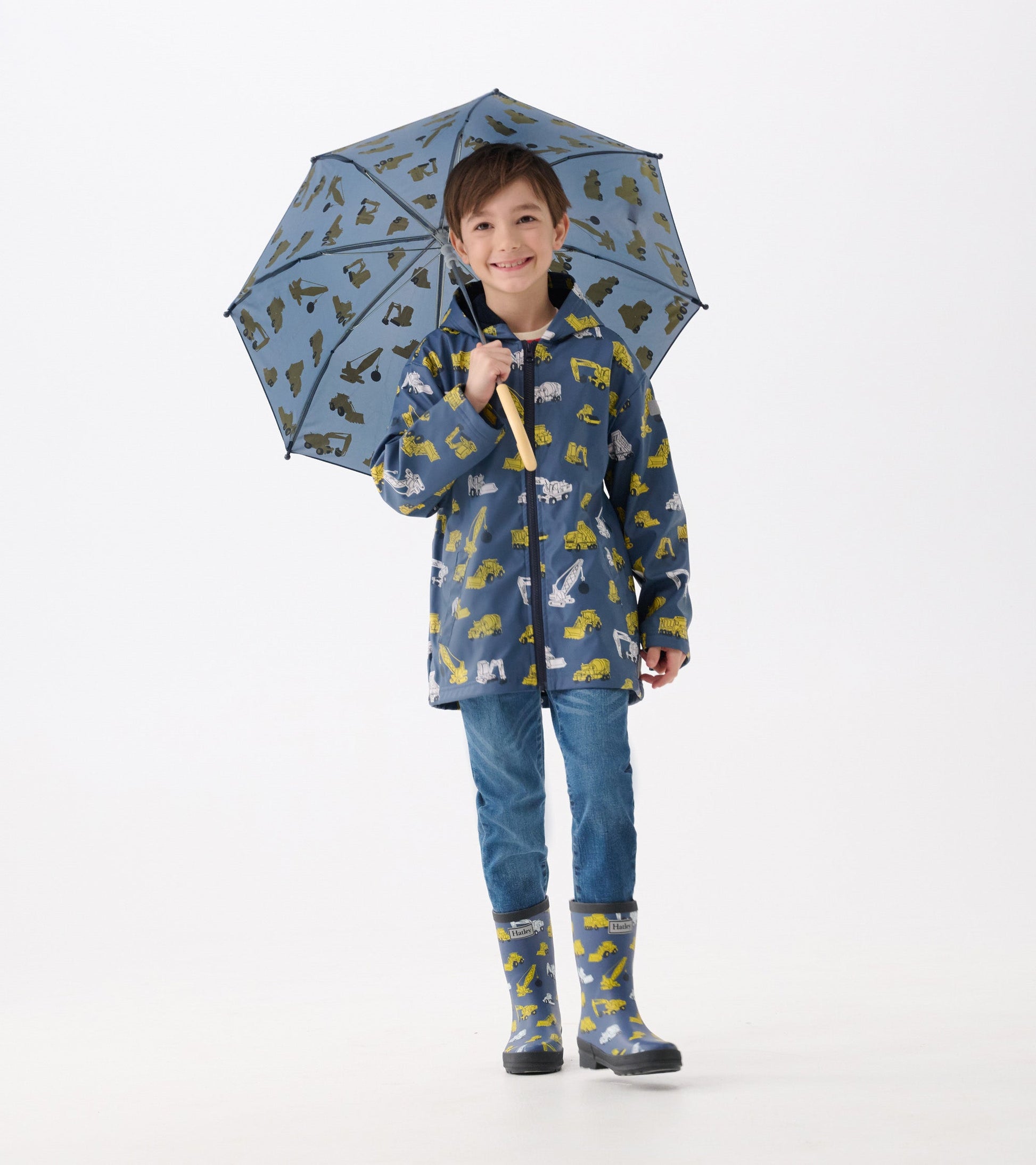 Blue zip-up rain jacket with construction vehicle patterns, worn by a boy holding a matching umbrella.