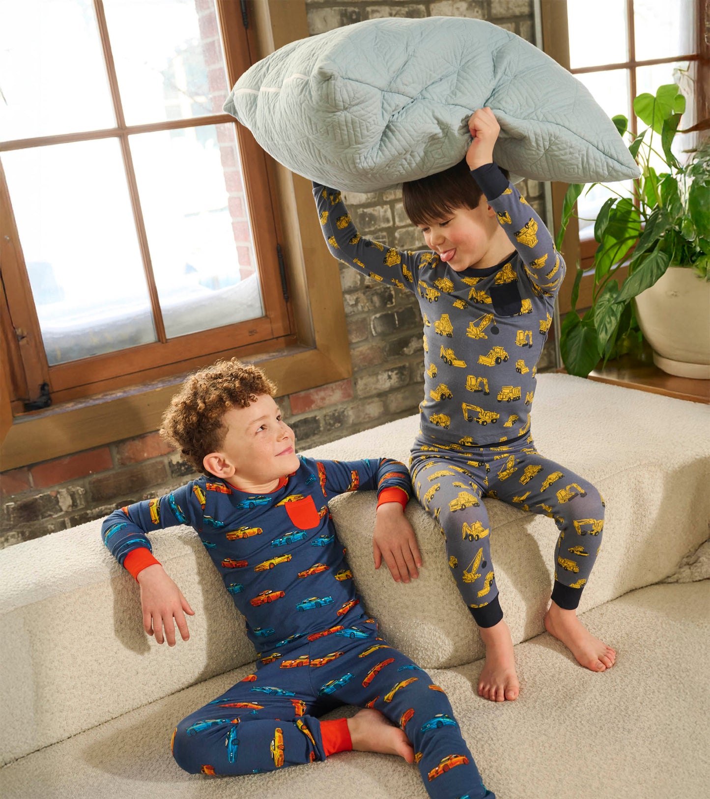 Two boys in long-sleeve bamboo pajamas with colorful car prints, one gray with yellow vehicles and one navy with multicolor…