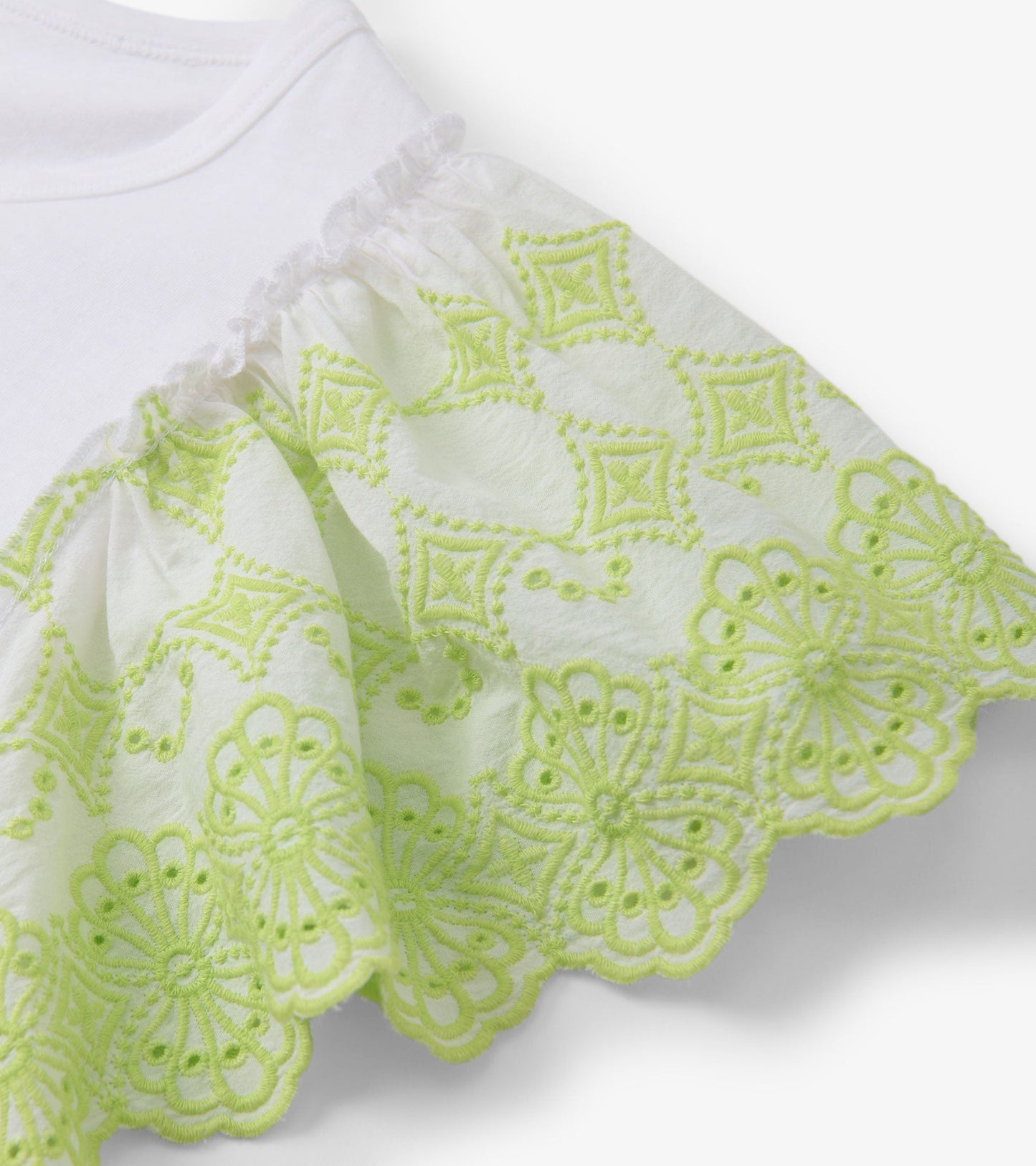 White tank top featuring eyelet sleeves with intricate green embroidery along the hem.