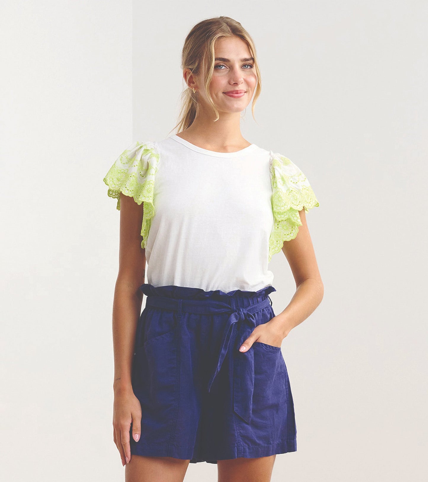 White tank top with eyelet lace sleeves in bright green, paired with navy shorts, worn by a smiling model.