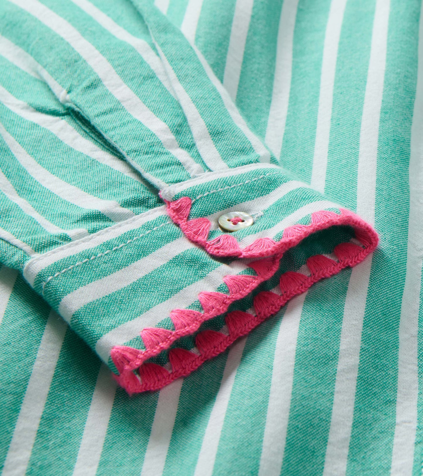 Close-up of mint green and white striped dress cuff with pink scalloped trim and button detail