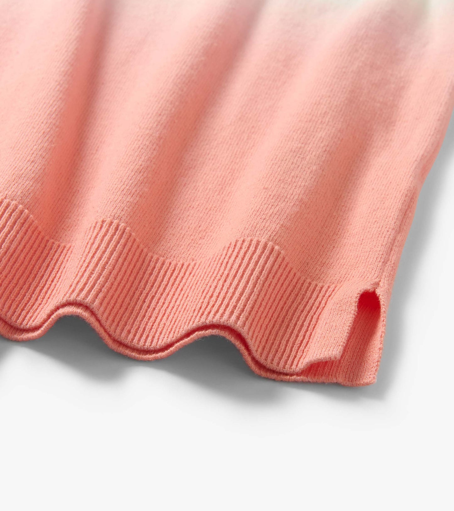 Close-up of a coral pink knit tee hem with scalloped edge and ribbed trim