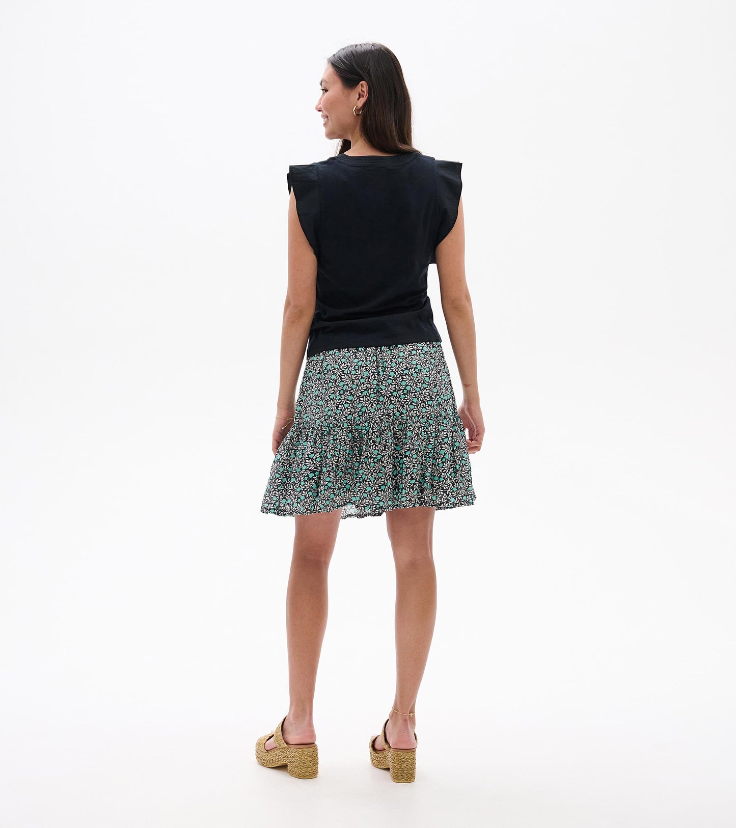 Back view of a black sleeveless tank top with ruffled shoulders and a teal-and-white floral skirt pattern.
