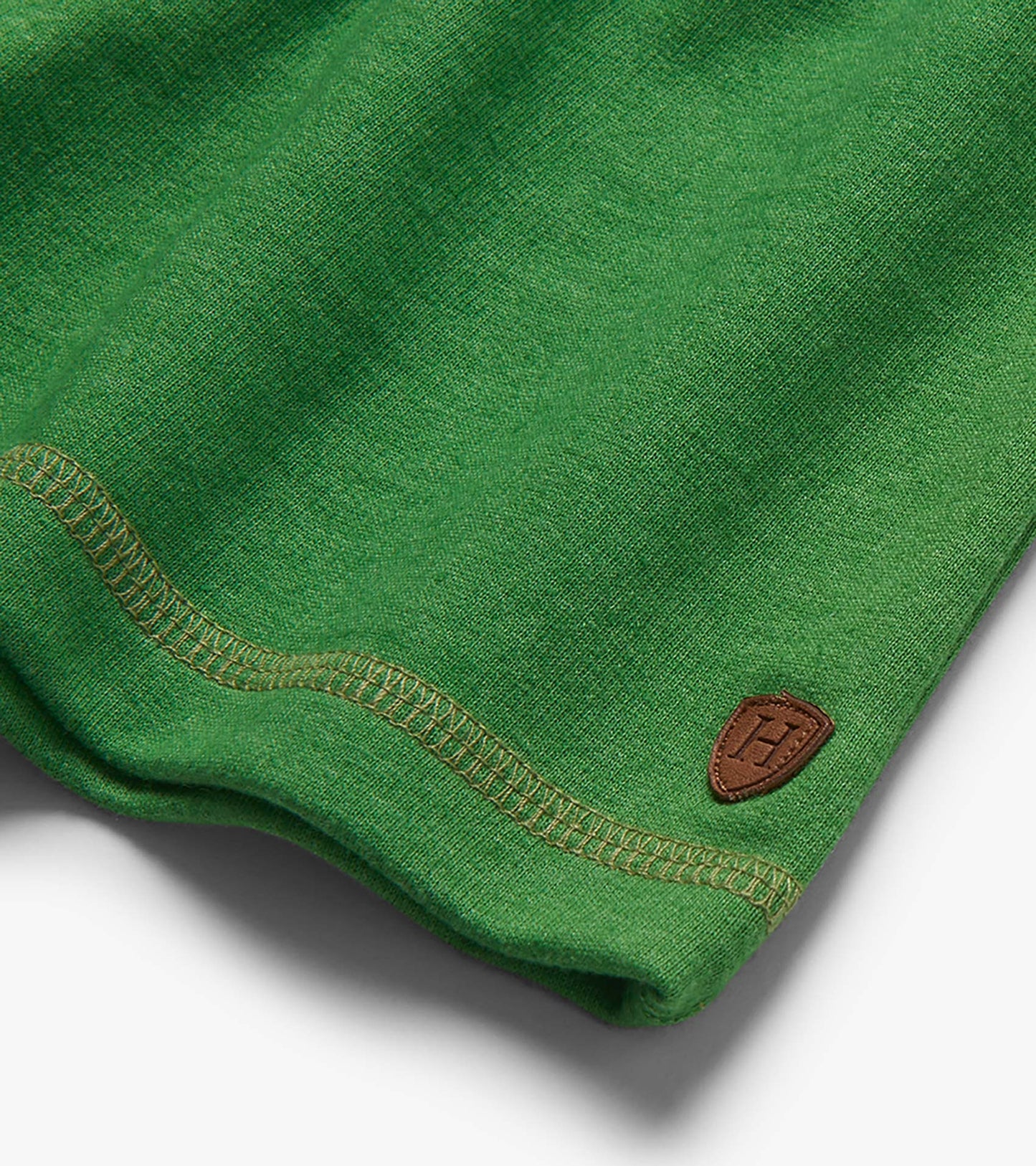 Close-up of green knit shorts hem with stitched seam and small brown patch logo